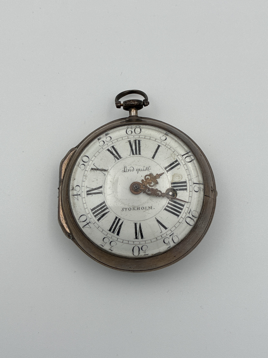 Fickur med urtavla av vit emalj med romerska siffror för timmar och arabiska siffror för minuter. Även signerat Lindquist Stockholm i svart. Urverket signerat "Jh Lindquist Stockholm N: 328" och avser hovurmakare Johan Lindquist (1728-1779). 

Boett av silver med stämplar: 
Mästarstämpel: IL = Johan Lindqvist 
Årsbokstav: E = 1763
Kattfot/tre kronor