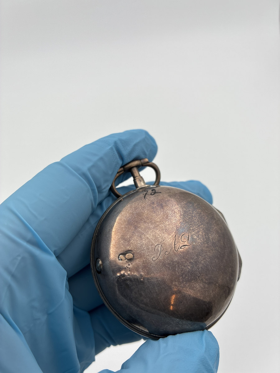 Fickur med osignerat urverk. Inner- och ytter boett av silver med brittiska stämplar. 

Innerboett:
Gående lejon = stämpel för silverhalt
Årsstämpel C = 1758
Ortsstämpel krönt leopardhuvud = London
Namnstämpel S.P

Ytterboett: 
Årsstämpel D = 1759
Ortsstämpel krönt leopardhuvud = London
Namnstämpel S.P