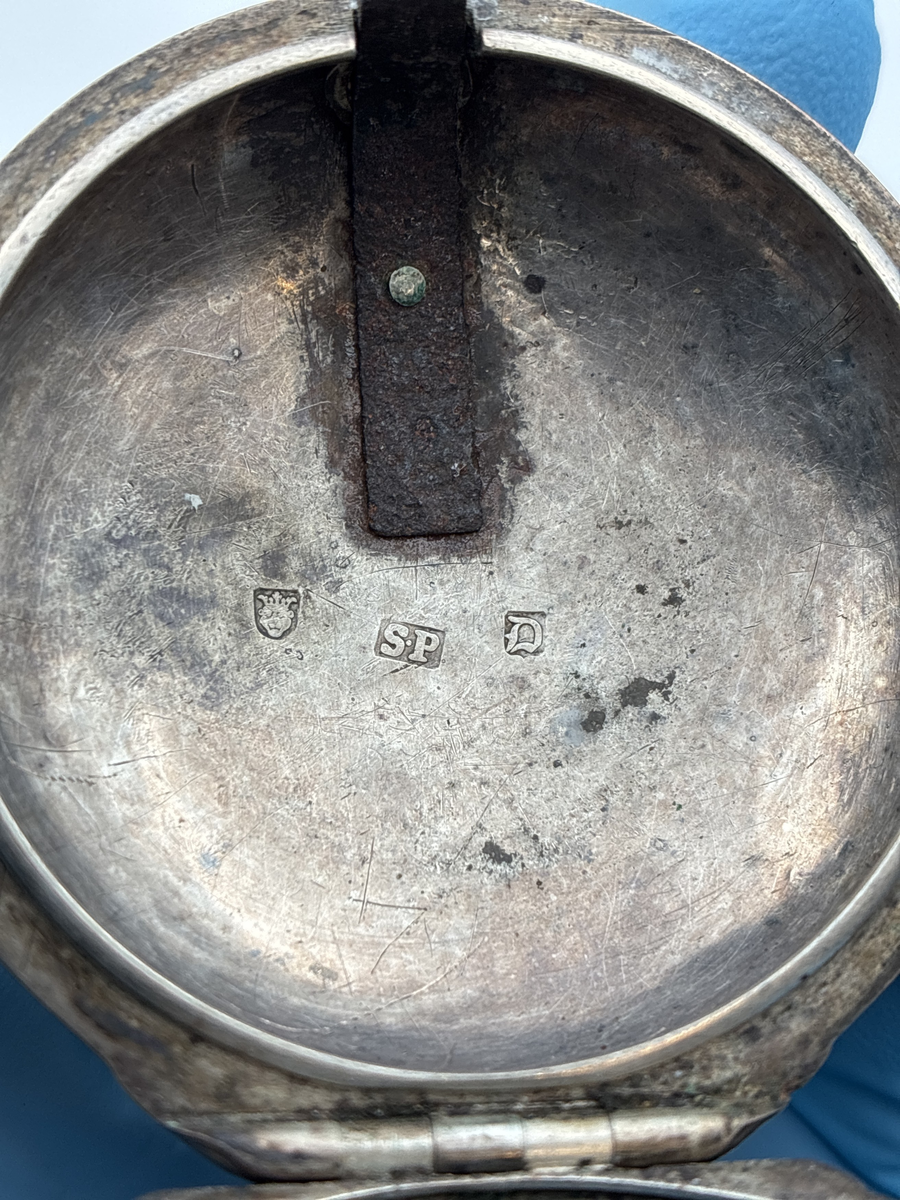 Fickur med osignerat urverk. Inner- och ytter boett av silver med brittiska stämplar. 

Innerboett:
Gående lejon = stämpel för silverhalt
Årsstämpel C = 1758
Ortsstämpel krönt leopardhuvud = London
Namnstämpel S.P

Ytterboett: 
Årsstämpel D = 1759
Ortsstämpel krönt leopardhuvud = London
Namnstämpel S.P