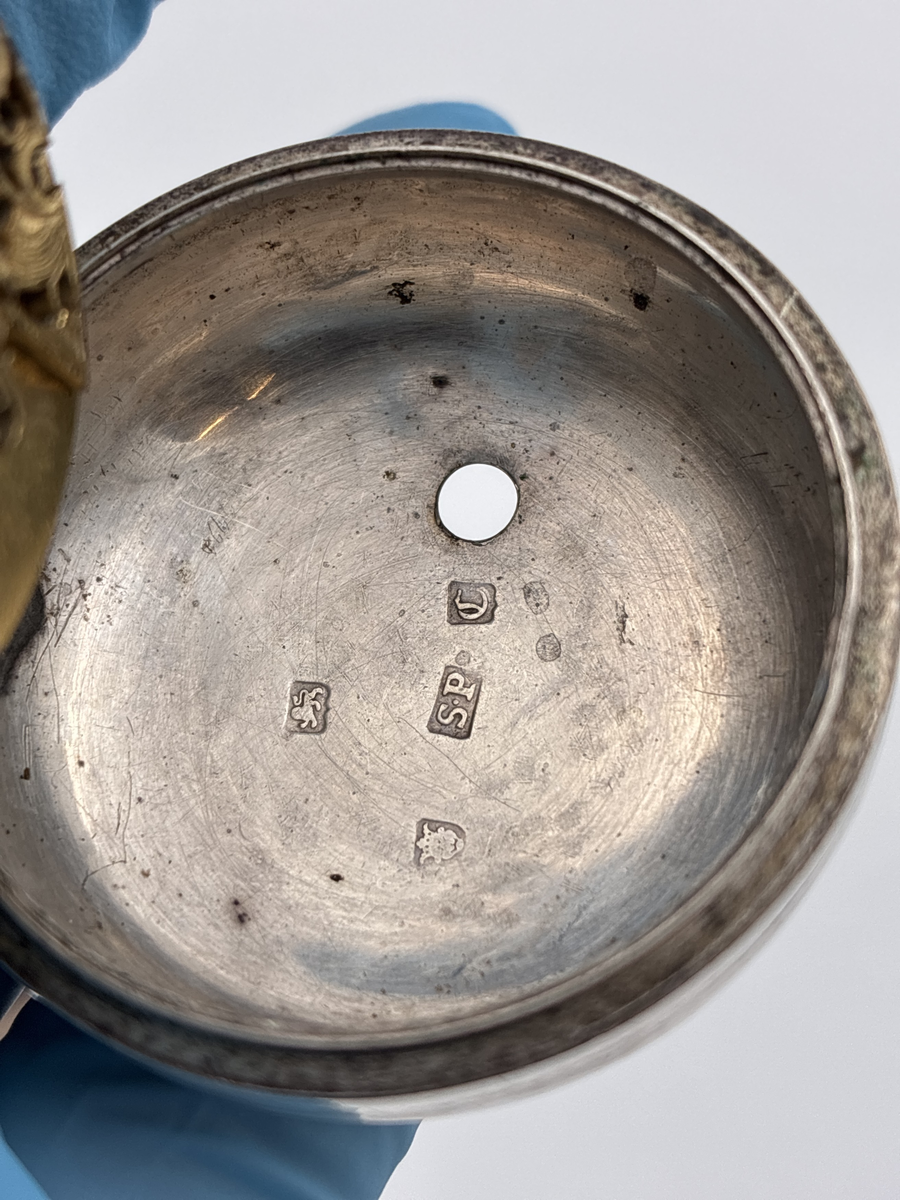 Fickur med osignerat urverk. Inner- och ytter boett av silver med brittiska stämplar. 

Innerboett:
Gående lejon = stämpel för silverhalt
Årsstämpel C = 1758
Ortsstämpel krönt leopardhuvud = London
Namnstämpel S.P

Ytterboett: 
Årsstämpel D = 1759
Ortsstämpel krönt leopardhuvud = London
Namnstämpel S.P