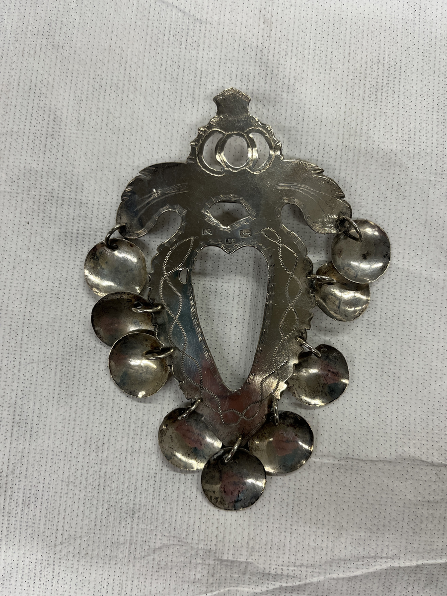 Hjärtformad bröstsölja med nio skålformade hängen.

Stadsstämpel: Hjorten= Alingsås
Årsstämpel: Y4= 1853
Mästarstämpel: AB= Anders Bäck