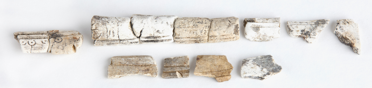 Ca 30 kamfragment tillhörande en trelagerskam med smal skena. Vissa är sammanförda och ihopklistrade. Dekoren består av två kantlinjer och punktcirklar.