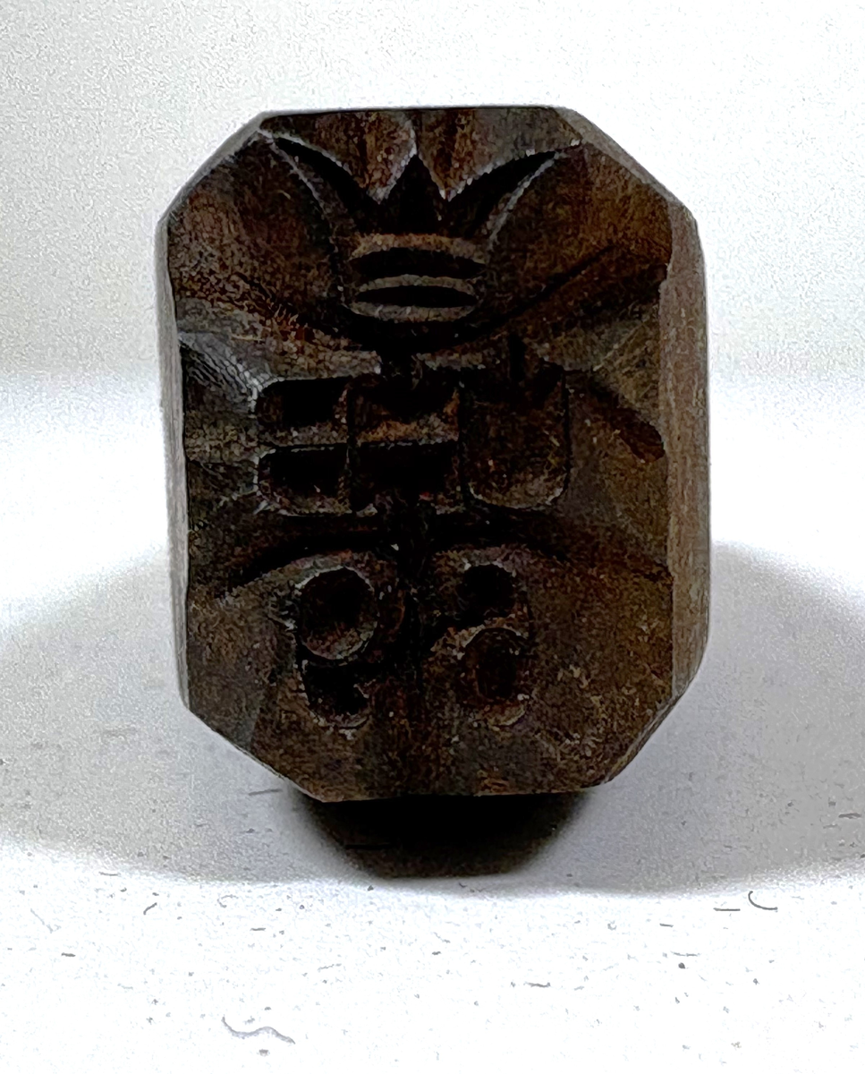 Ett körnslag. Rektangulärt metallstycke som har en rundad slagyta i ena änden, och är avsmalnande i andra änden med texten "UHB 69" krönt med en kungakrona.