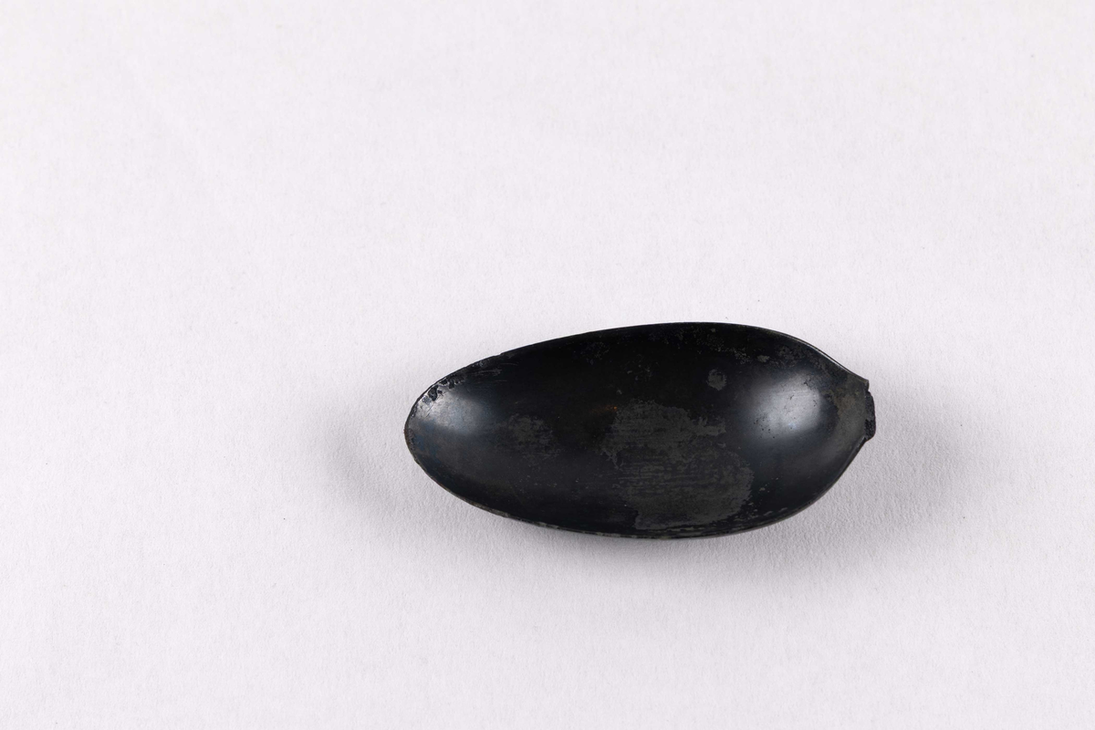 Del av skje bestående av hode funnet ved skipet AKERENDAM som forliste på Runde i 1725. Enkel dekor på ytterside av hode, skaftet mangler.