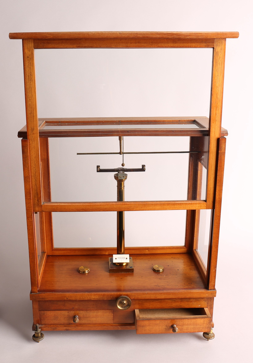 Analysevekt montert i trekasse med glassvegg og -tak, to skuffer i sokkelen (tilbehør inne). Glassveggene i front og på baksiden kan tas bort / fungerer som "skivedør". Skivedøren i front kan også festes halvåpent. Under kassen finnes det to justerbare føtter på forsiden, og en på baksiden. Vektstativet er fast montert i kassen, samt veiemekanisme, to justeringshjul (en i front og en på høyre siden) og vektskala. Løse deler til miligramsvekten er presisjons-vektstang, to oppheng og to vektskål. Som svært presist måleinstrument ble analysevekten brukt til å bestemme massen av små prøver med høy grad av presisjon. Denne vekten her lingner på typen av analysevekt som er produsert ved "Paul Bunge, Fabrik wissenschftlicher Waagen" i Hamburg / Tyskland, rundt 1930-tallet.