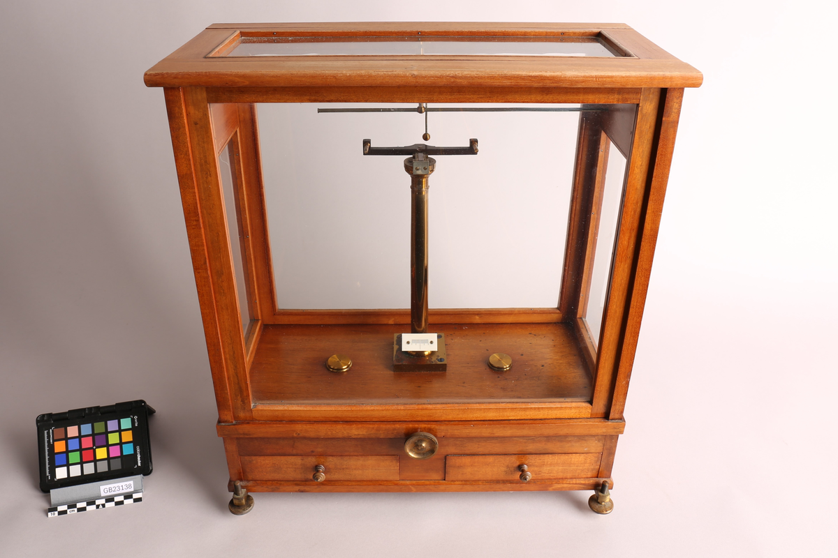 Analysevekt montert i trekasse med glassvegg og -tak, to skuffer i sokkelen (tilbehør inne). Glassveggene i front og på baksiden kan tas bort / fungerer som "skivedør". Skivedøren i front kan også festes halvåpent. Under kassen finnes det to justerbare føtter på forsiden, og en på baksiden. Vektstativet er fast montert i kassen, samt veiemekanisme, to justeringshjul (en i front og en på høyre siden) og vektskala. Løse deler til miligramsvekten er presisjons-vektstang, to oppheng og to vektskål. Som svært presist måleinstrument ble analysevekten brukt til å bestemme massen av små prøver med høy grad av presisjon. Denne vekten her lingner på typen av analysevekt som er produsert ved "Paul Bunge, Fabrik wissenschftlicher Waagen" i Hamburg / Tyskland, rundt 1930-tallet.