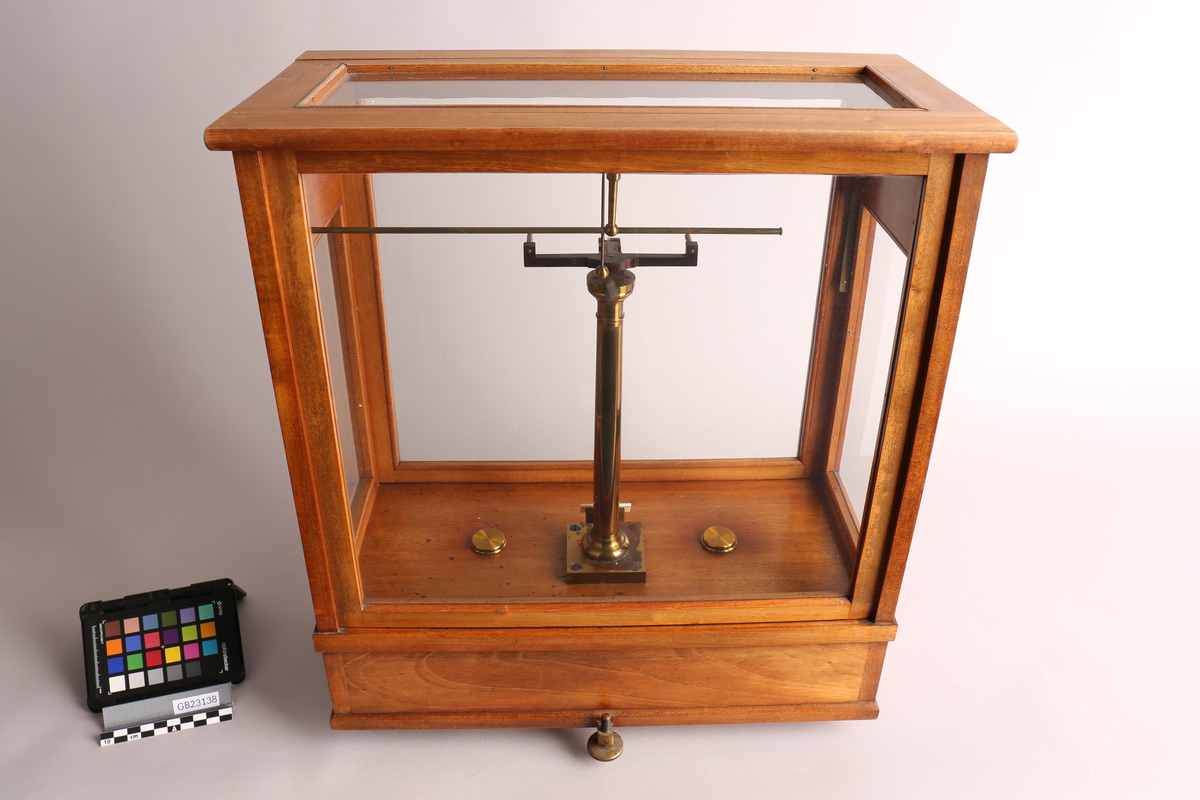 Analysevekt montert i trekasse med glassvegg og -tak, to skuffer i sokkelen (tilbehør inne). Glassveggene i front og på baksiden kan tas bort / fungerer som "skivedør". Skivedøren i front kan også festes halvåpent. Under kassen finnes det to justerbare føtter på forsiden, og en på baksiden. Vektstativet er fast montert i kassen, samt veiemekanisme, to justeringshjul (en i front og en på høyre siden) og vektskala. Løse deler til miligramsvekten er presisjons-vektstang, to oppheng og to vektskål. Som svært presist måleinstrument ble analysevekten brukt til å bestemme massen av små prøver med høy grad av presisjon. Denne vekten her lingner på typen av analysevekt som er produsert ved "Paul Bunge, Fabrik wissenschftlicher Waagen" i Hamburg / Tyskland, rundt 1930-tallet.