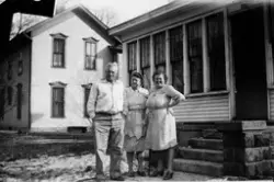 En mann og to kvinner står utenfor et hus med innglasset ver