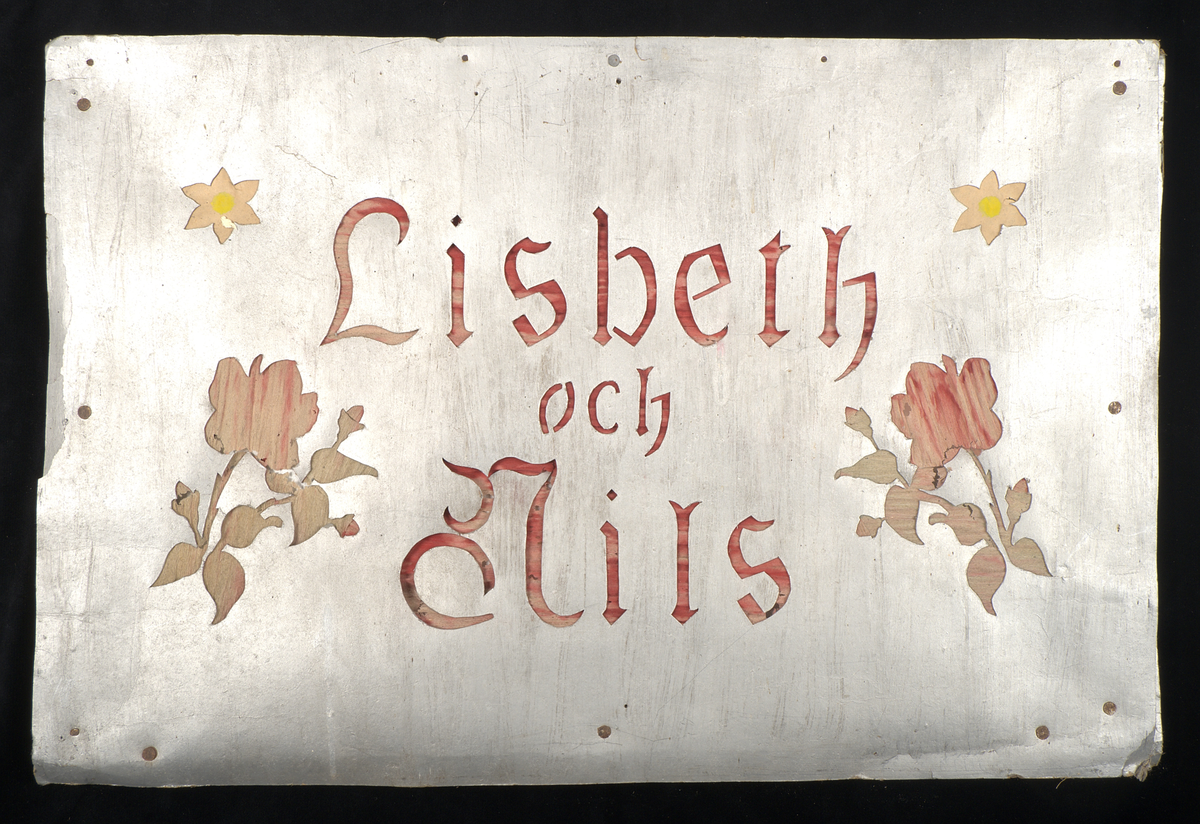 Bröllopslykta/transparang av kraftigt silverfärgat papper spänt över träram. I pappret finns skurna dekorationer i form av florala mönster, symboler och text. Bakom de utskurna partierna har silkespapper i grönt, rött och gult monterats. På framsidan återfinns texten: "Lisbeth och Nils", på baksidan: "Lycka och wälgång".