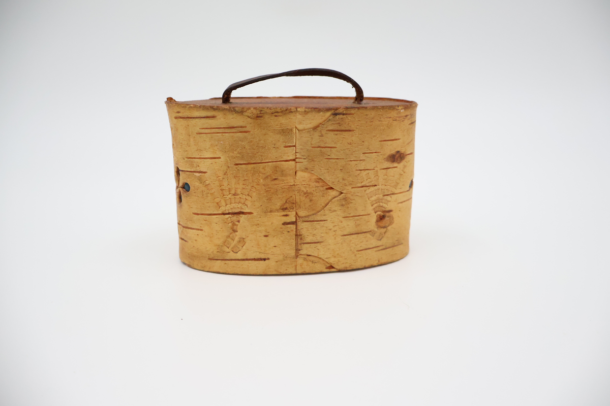 Oval näverburk med lock. Liten. Nävret är tampat stående. Nävret är pålimmat på bottenplattan i trä. Även locket består av trä och har ett handtag i läder. Läderremmen är trädd genom två hål i locket och på lockets insida avslutas remmen med två knutar. Burken har utstansade dekorationer i form av solfjädrar, romber, blommor och en stjärna. Burken består av två lager näver och emellan nävret är blått tyg inlagt som skymtar fram i stjärnan och blommorna. Burken är i relativt gott skick.