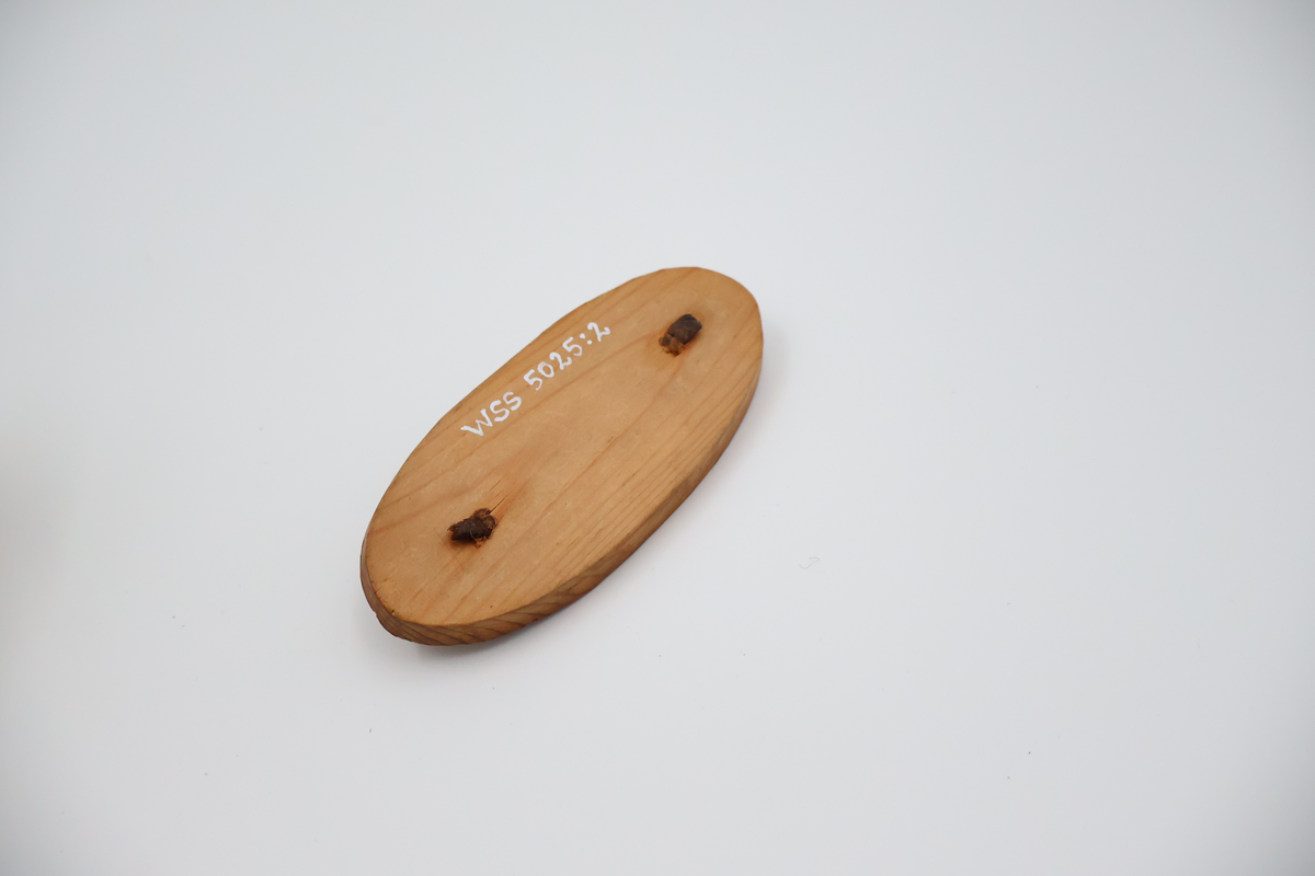 Oval näverburk med lock. Liten. Nävret är tampat stående. Nävret är pålimmat på bottenplattan i trä. Även locket består av trä och har ett handtag i läder. Läderremmen är trädd genom två hål i locket och på lockets insida avslutas remmen med två knutar. Burken har utstansade dekorationer i form av solfjädrar, romber, blommor och en stjärna. Burken består av två lager näver och emellan nävret är blått tyg inlagt som skymtar fram i stjärnan och blommorna. Burken är i relativt gott skick.