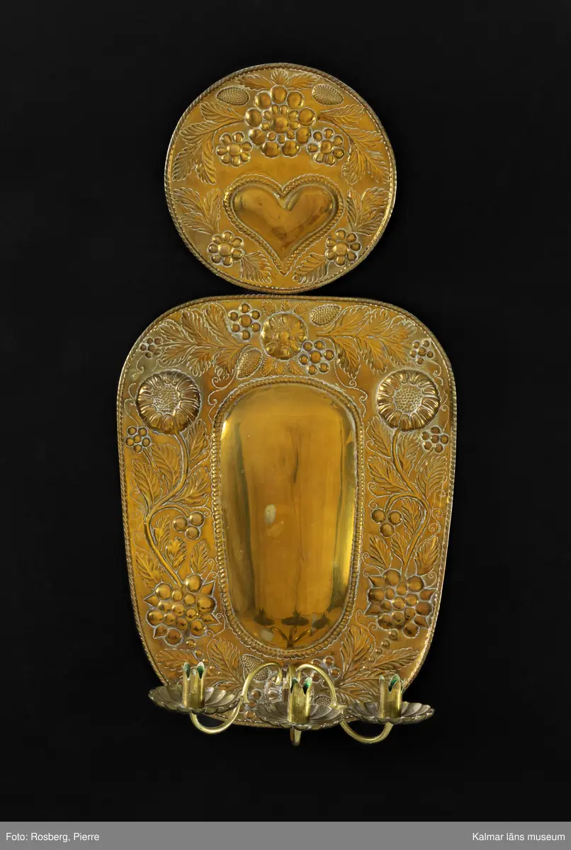 KLM 28652:11:1-2. Lampett. Två stycken. Av driven mässing. I mitten konvex oval form, runt om ovalen pressat mönster i form av blommor och blad. Upptill rund reflektorsplåt med pressat mönster med blommor, blad samt ett hjärta. Löstagbar ljusarm med ljushållare för tre ljus.