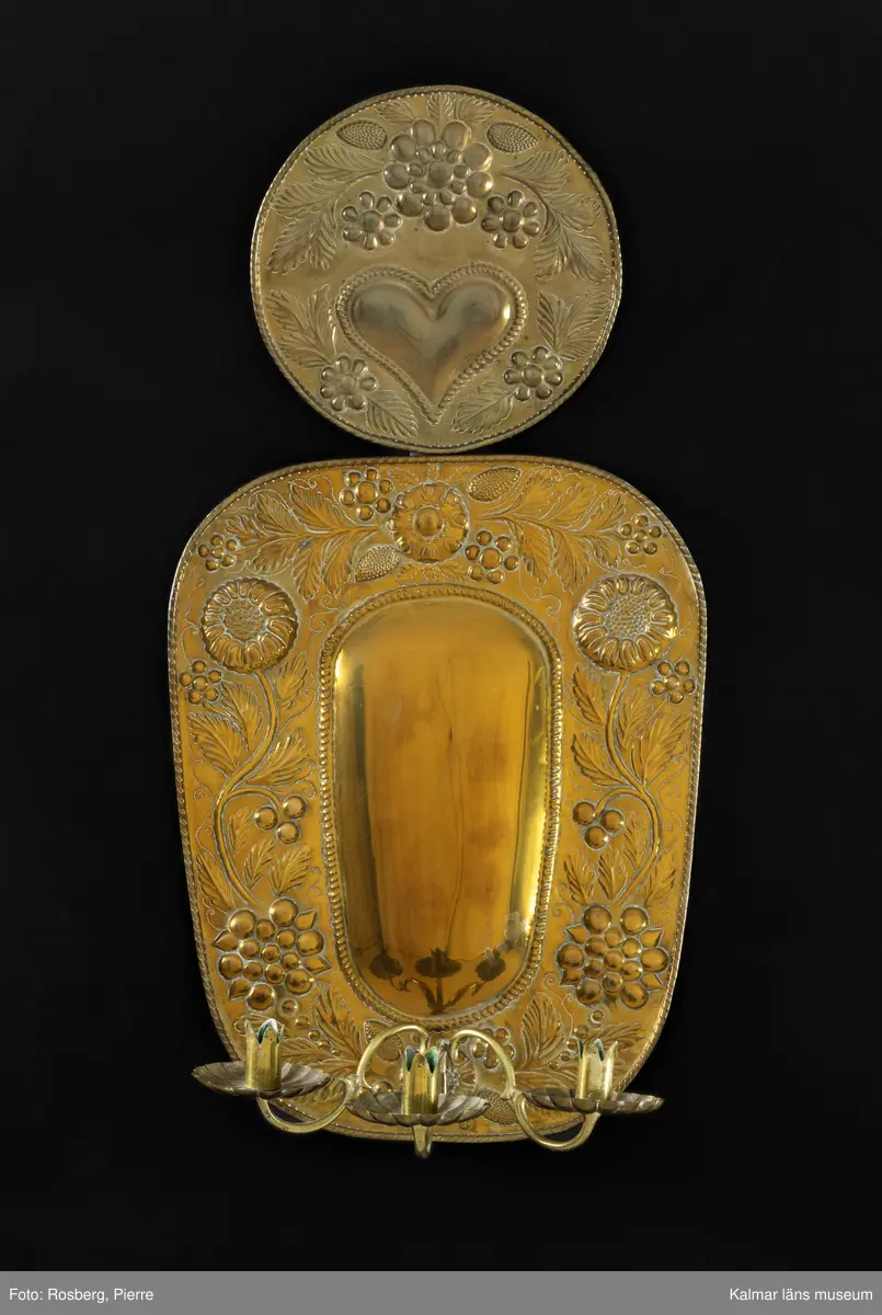 KLM 28652:11:1-2. Lampett. Två stycken. Av driven mässing. I mitten konvex oval form, runt om ovalen pressat mönster i form av blommor och blad. Upptill rund reflektorsplåt med pressat mönster med blommor, blad samt ett hjärta. Löstagbar ljusarm med ljushållare för tre ljus.