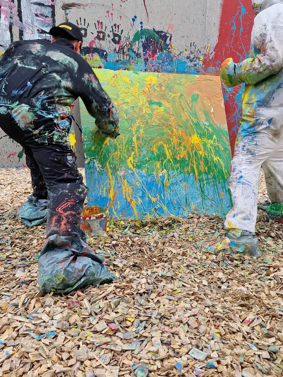 Två barn målar på en tavla med actionpainting.