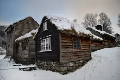 Museumstunet med snø. Snø ligger på torvtak og istapper henger ned frå taket.