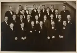 Gruppefotografi. 28 menn i mørk dress og tversoversløyfe. Re