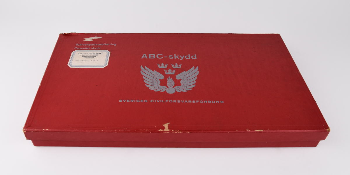 Röd låda i papp med texten "ABC-skydd SVERIGES CIVILFÖRSVARSFÖRBUND" "Självskyddsutbildning Personligt skydd" och en etikett med texten "STATENS JÄRNVÄGAR I DISTRIKTSKANSLIET Försvarsavdelningen STOCKHOLM Utbildningssats nr 3" 
Innehåller:
:1 Kartong.
:2 Kursplaner: Skydd mot kärnvapen; Skydd mot biologiska stridsmedel och mot stridsgaser.
:3 Särtryck: Radiakskydd.
:4 Särtryck: Medför atombombproven några genetiska risker?
:5 Särtryck: Vistelsen i skyddsrum bör planeras för 3 dygn.
:6 Särtryck: Radiakinstrument.
:7 Stillfilm: Kärnvapen I ( ljudband).
:8 Stillfilm: Kärnvapen I ( bildband).
:9 Stillfilm: Kärnvapen II (ljudband).
:10 Stillfilm: Kärnvapen II (bildband).
:11 Stillfilm: Biologisk krigsföring (ljudband).
:12 Stillfilm: Biologisk krigsföring (bildband). 
:13 Bildband: Skydd mot stridsgaser.