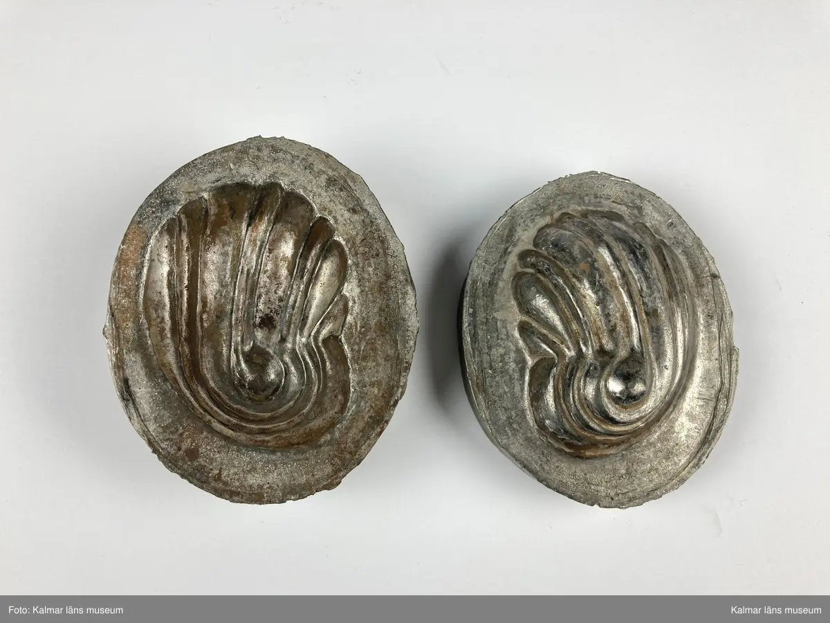 KLM 46890:23. Stans. 2 delar. För tillverkning av kakformar. Av bly. Stansen består av ett ovalt block med försänkning i form en oval kakform med vågigt mönster. Till stansen hör en kontra med kakformens form, denna passar försänkningen på stansen och lägges där i. Materialet som ska pressas läggs mellan stansens båda delar och försetts sedan med tyngd för att forma materialet. Kakform KLM 46890:20 har tillverkats med stansen.