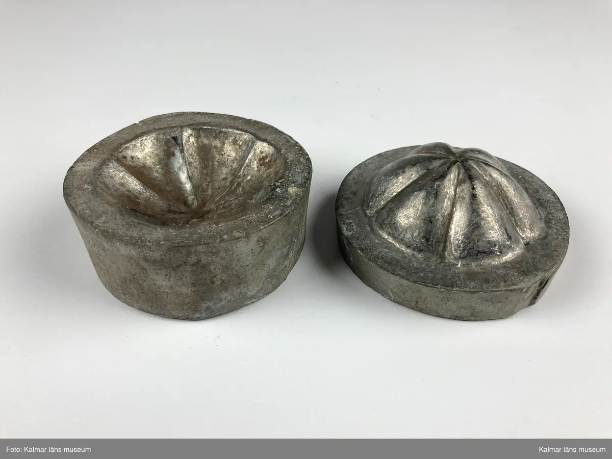 KLM 46890:24. Stans. 2 delar. För tillverkning av kakformar. Av bly. Stansen består av ett ovalt block med försänkning i form en rund kakform med vågigt mönster. Till stansen hör en kontra med kakformens form, denna passar försänkningen på stansen och lägges där i. Materialet som ska pressas läggs mellan stansens båda delar och försetts sedan med tyngd för att forma materialet. Kakform KLM 46890:21 har tillverkats med stansen.