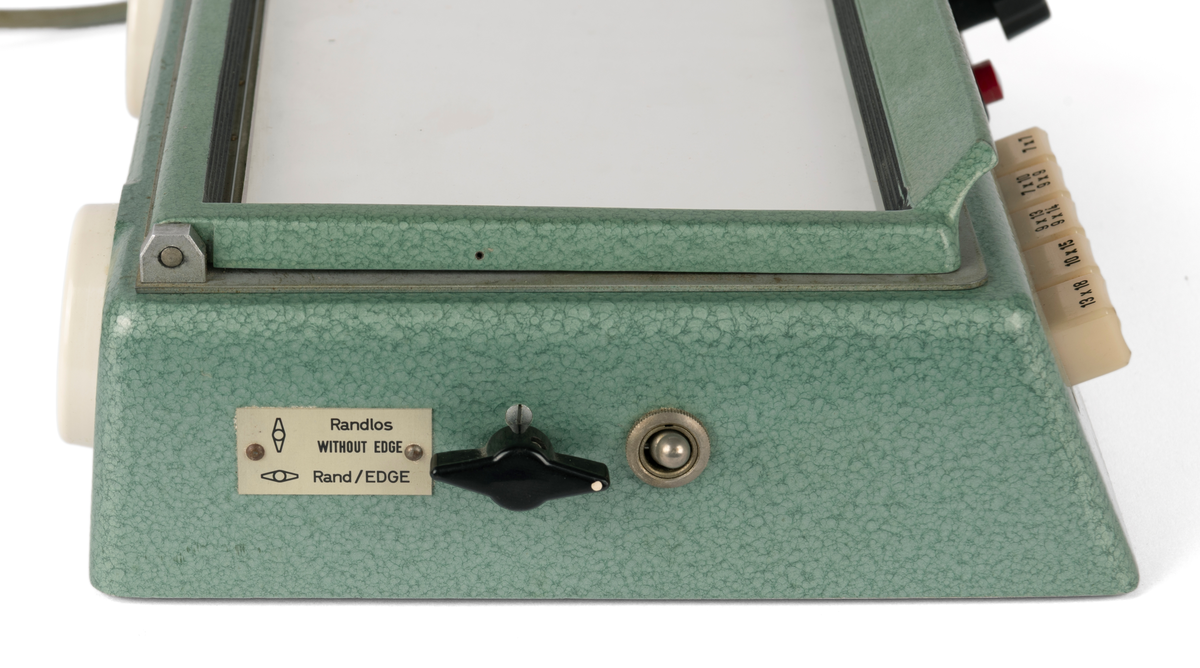 Kontaktkopieringsapparat med to straumfordelarar til prosjektor/ mørkeromslampe. Fleire innstilling- og justeringsknappar. Med tilhøyrande deksel i plast.