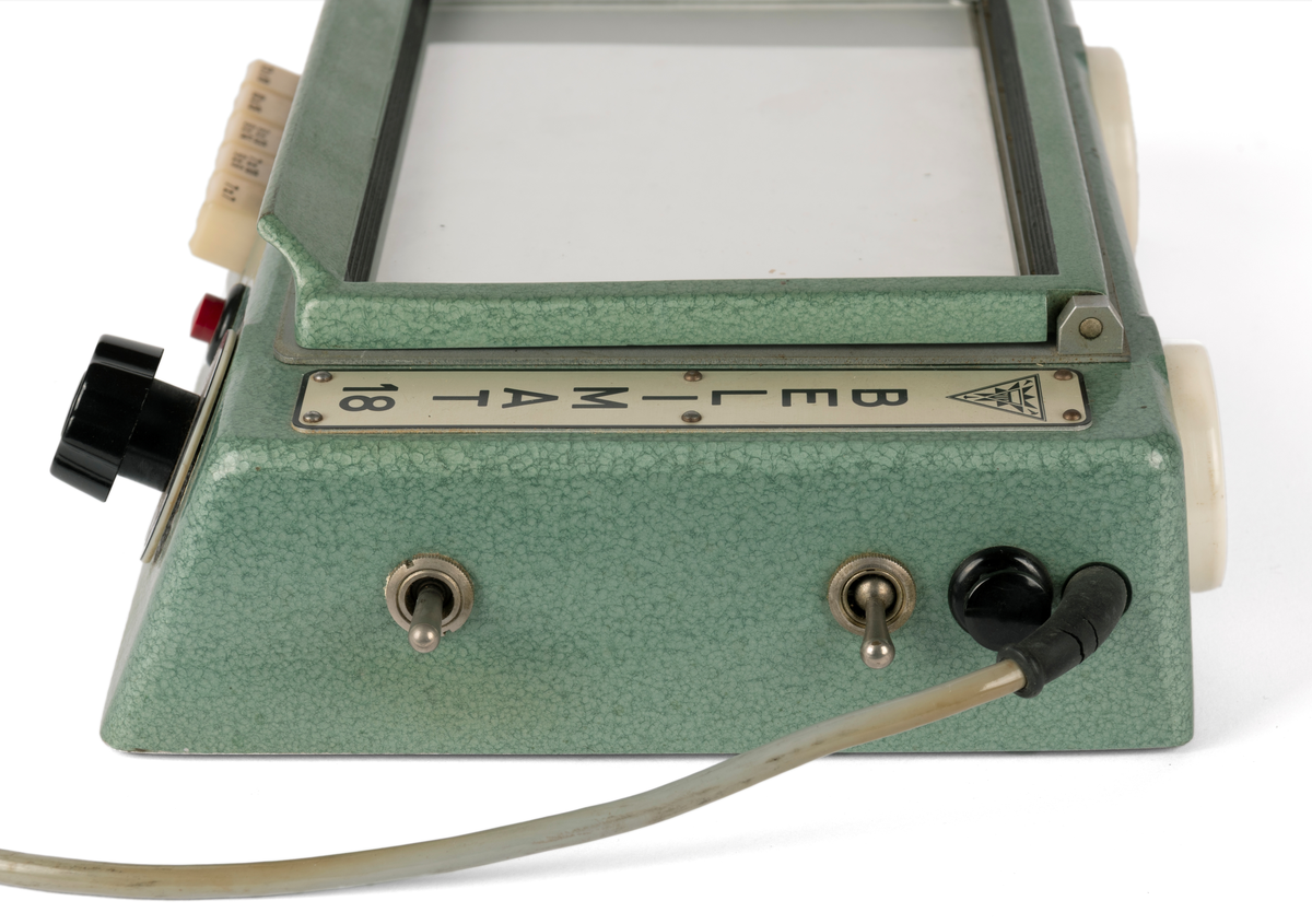 Kontaktkopieringsapparat med to straumfordelarar til prosjektor/ mørkeromslampe. Fleire innstilling- og justeringsknappar. Med tilhøyrande deksel i plast.