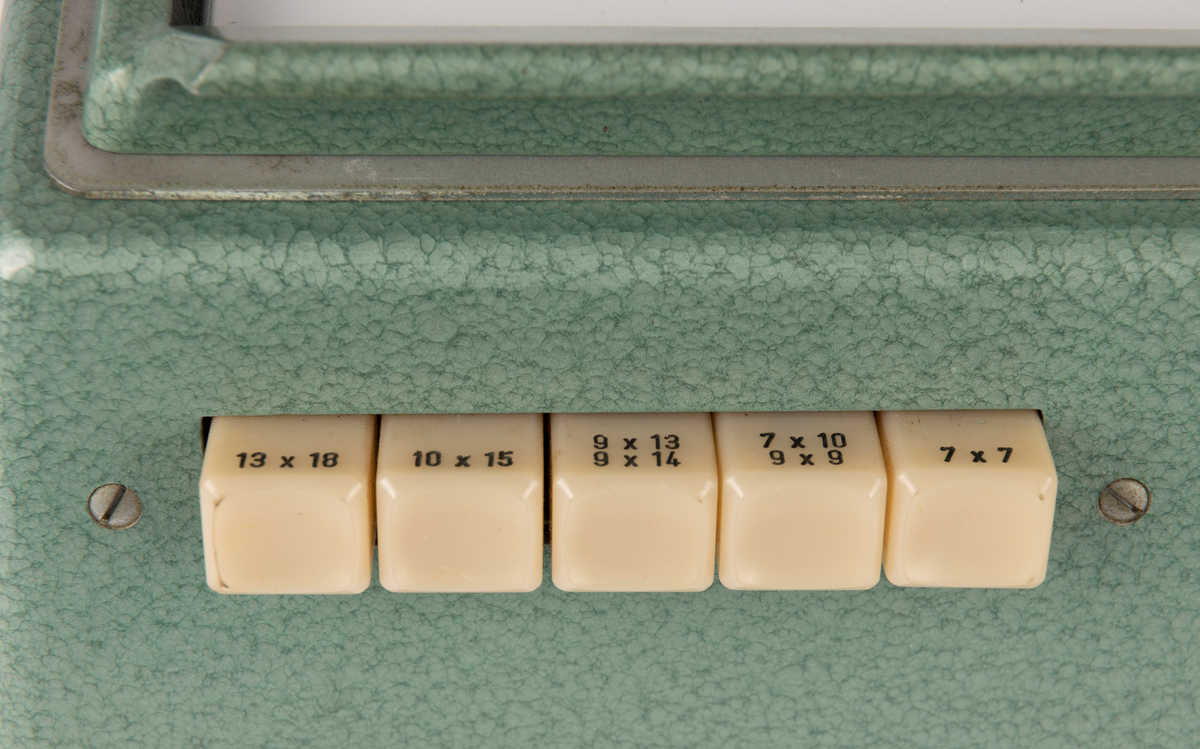 Kontaktkopieringsapparat med to straumfordelarar til prosjektor/ mørkeromslampe. Fleire innstilling- og justeringsknappar. Med tilhøyrande deksel i plast.