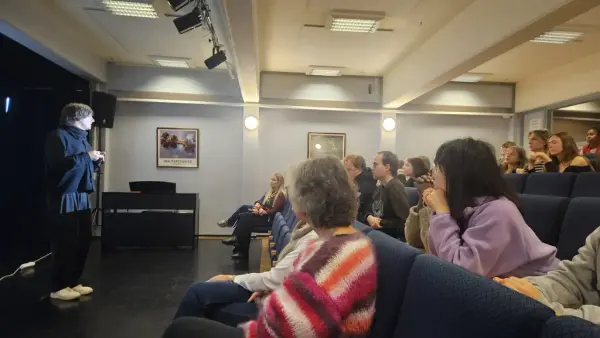 En mann står til venstre i et auditorium og snakker mot publikum som sitter til høyre. 