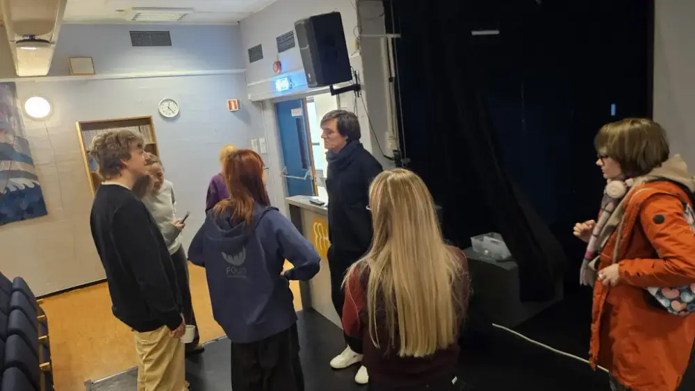 En gruppe unge mennesker står og snakker med hverandre i et auditorium.