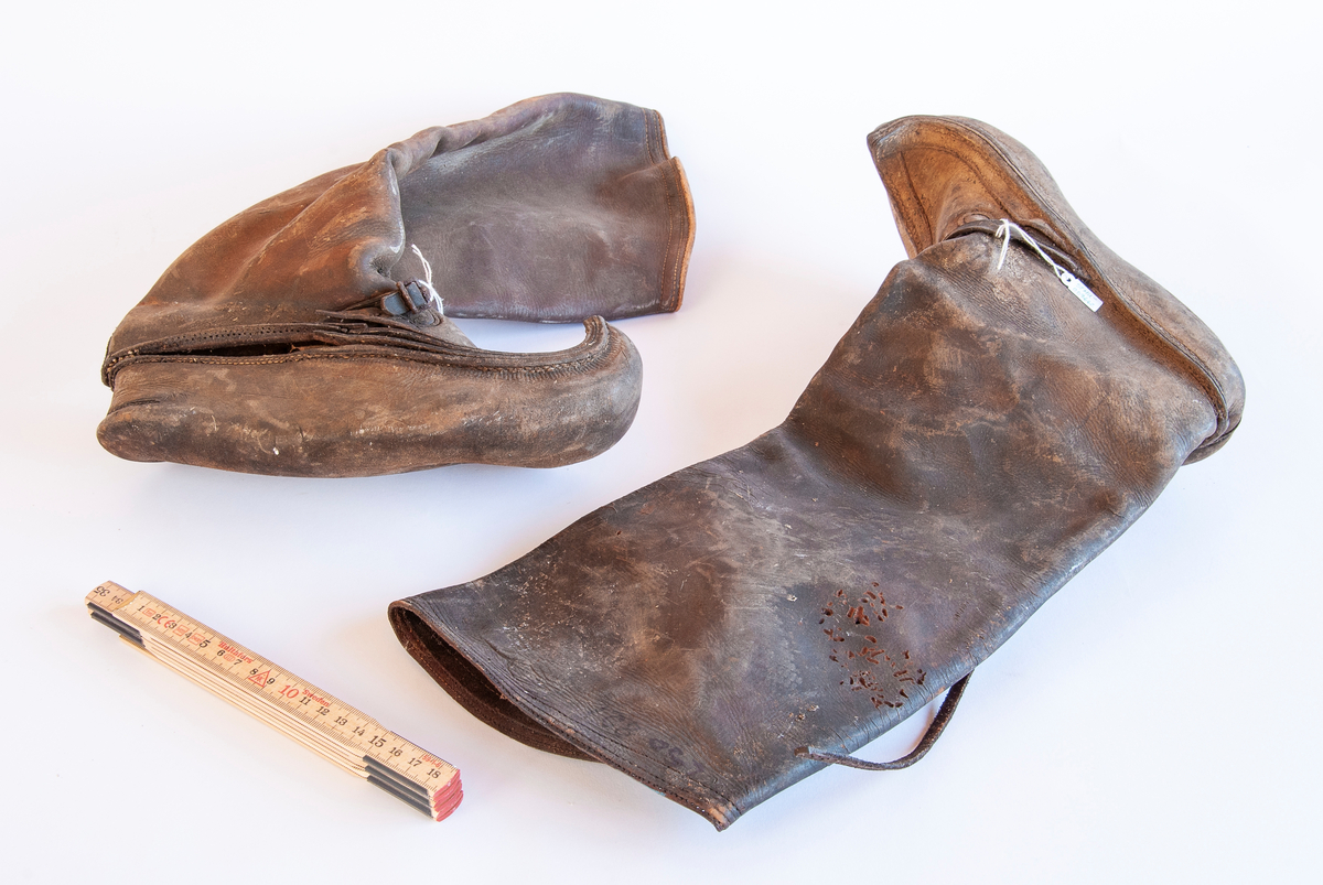 Et par bjeksoer (finnsko) sydd av lær. Foten er bøyd opp foran til en "nebb". Lange skaft. Sprukket i sømmene. Lærreim med spenne over foten.