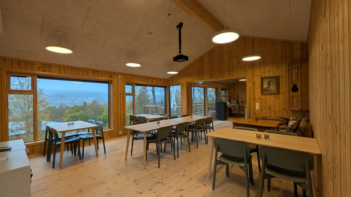 Bilde av kaferommet på Trysil-bygdetun. Det er satt opp et langbord på midten og bord inntil vinduene på høyre side.