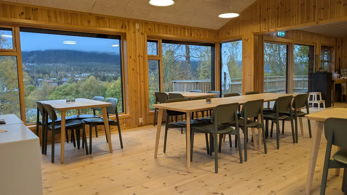 Bilde av kaferommet på Trysil bygdetun. Det er satt opp et langbord på midten og enkeltbord inntil vinduene. Lerret til prosjektoren er rullet ned