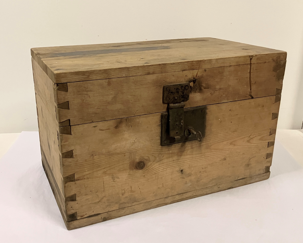 Målselv: Klasrommet: Lundberg: Trekiste. Trekvit. Form: Rektangulær kube. Sinket i hjørnene. Plant lokk med metallhengsler og låseskasse felt inn i front.