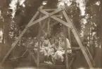Tre unga kvinnor och en pojke i en trädgårdsgunga.
Trol. bl a t.v. Kristina Nilsson (1898-1973) och hennes bror Benno (1904-1995), Gårdsby säteri.