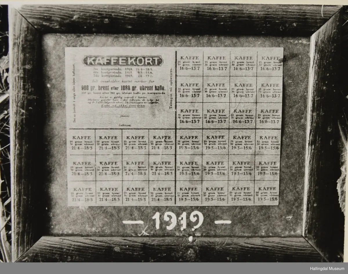 Rasjoneringskort til kaffi. Limt på mørk grå kartong. Skrive årstalet 1919 med kvit skrift under kortet. Mørk brun treramme.