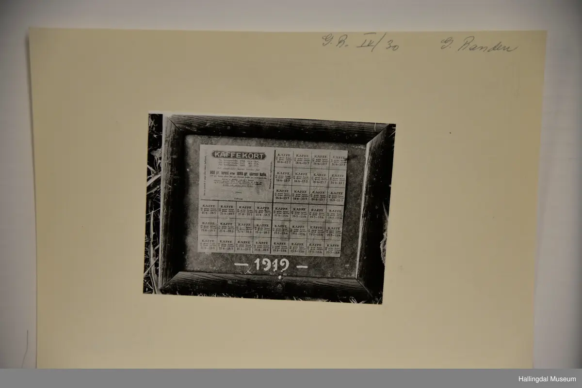 Rasjoneringskort til kaffi. Limt på mørk grå kartong. Skrive årstalet 1919 med kvit skrift under kortet. Mørk brun treramme.