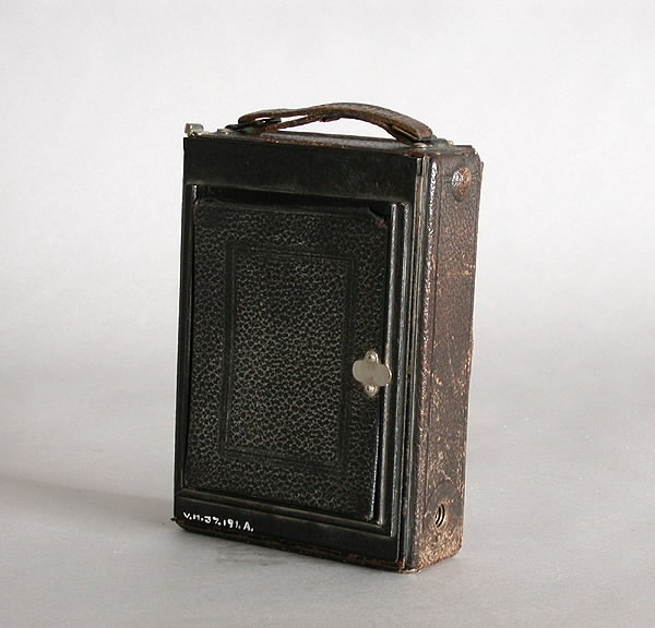 "Kamera-bälg.a) Rektangulär plåtlåda överdragen med svart vaxduk. Ena långsidan fälls utoch bälg med optik dras fram. Optiken kan förskjutas i höjd- och sidoled.Märke: ""Ica"" . Modell: ""Trona 210"".Längd (öppen): 27 cm. Längd (stängd): 15,5 cm.Bredd (öppen): 11 cm.Bredd (stängd): 11 cm.Höjd (öppen): 15,5 cm.Höjd (stängd): 5 cm.b) Löstagbart bakstycke med matt skiva. Kassett för glasplåtar 9x12 cm saknas.Mått: 10x15 cm.c) Trådutlösare, metallsnodd överdragen med svart textil.Längd: 27,5 cm.d) Gulgrön-filter av glas i en metallram som spänns fast runt objektivet.Höjd: 1,5 cm.Diameter: 3,8 cm.e) Oval pung i brunt skinn, försluts med en dragkedja. Rymmer trådutlösarenoch filtret.Bredd: 9 cm.Höjd: 6 cm."