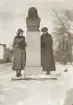 Två kvinnor på vinterpromenad, avfotograferade vid Carl von Linnés byst i Linnéparken, Växjö.
Bakom dem skymtar några hus längs Linnégatan.