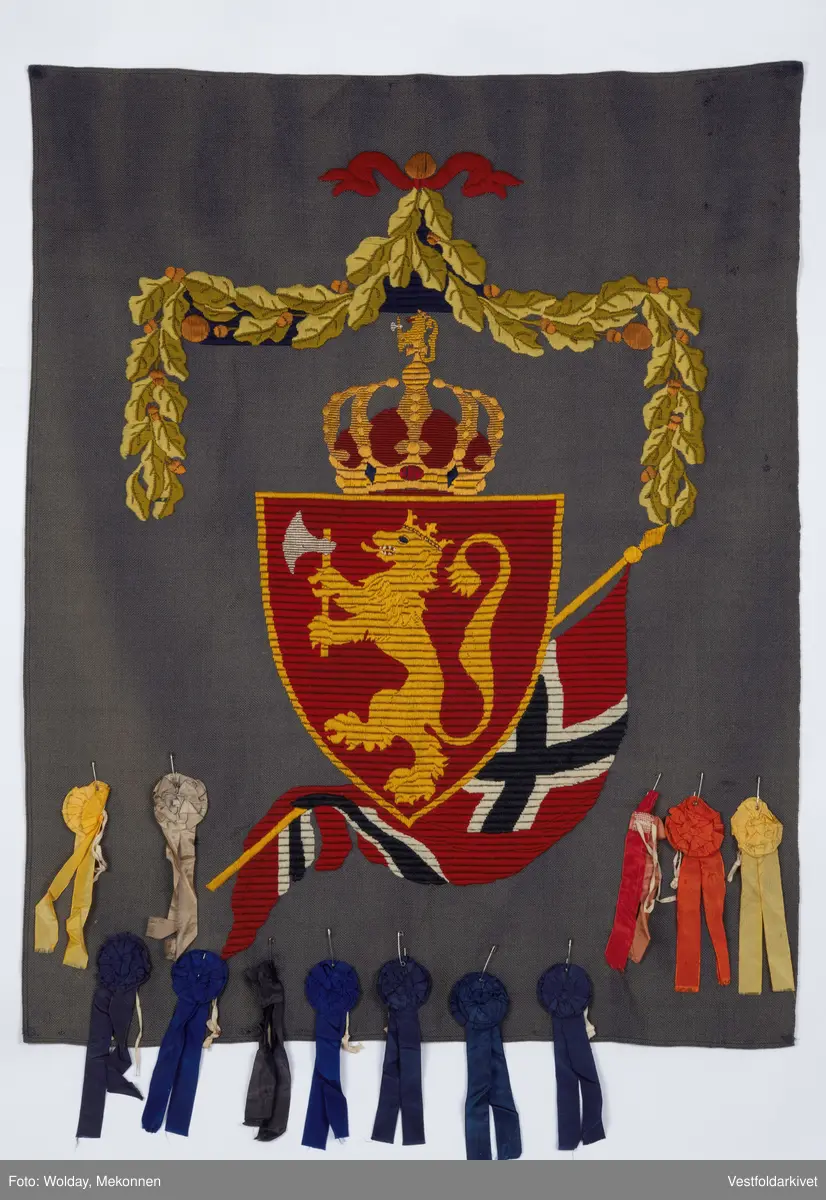 Blått veggteppe med riksvåpenet, påfestet rosetter 