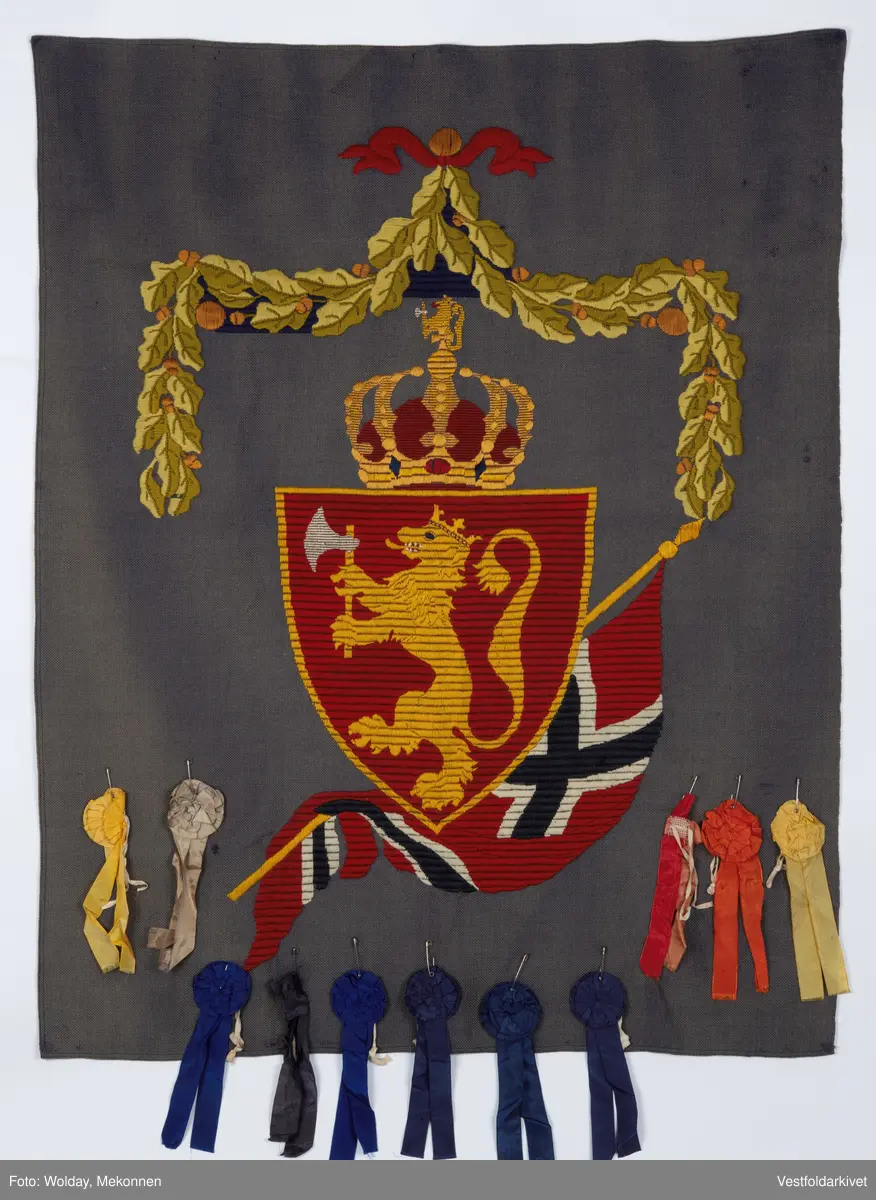 Blått veggteppe med riksvåpenet, påfestet rosetter 