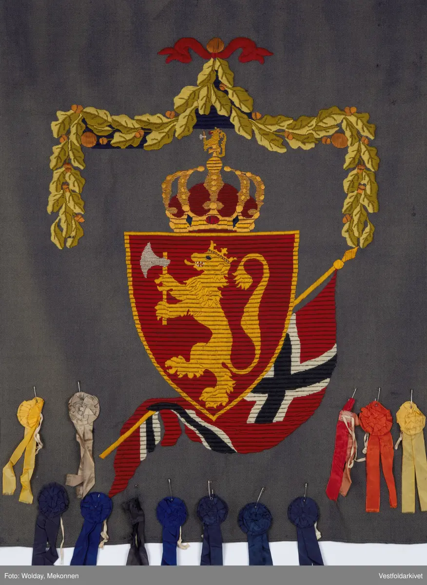 Blått veggteppe med riksvåpenet, påfestet rosetter 