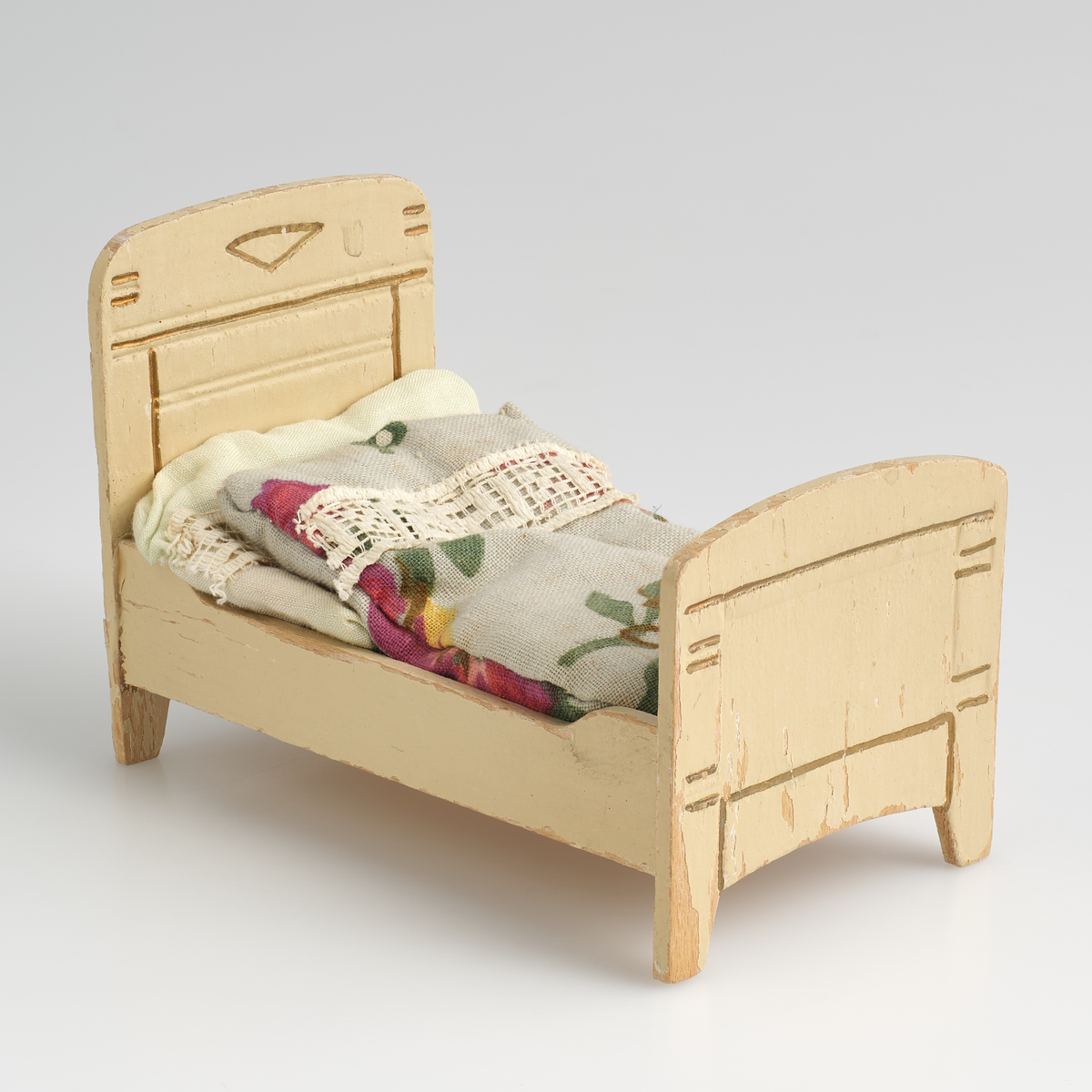 Leketøysseng til dukkehus, tilhørt en lekestue på 1930-tallet.
Sengen består av tre individuelle løse deler; sengeramme, pute og dyne.
Sengerammen er av tre, malt kremhvit, og limt sammen av 5 deler; to endesider, to sengekanter, og en plate. 
Endesiden ved sengens hodeende, er dekorert med et inngravert mønster malt i gull, mønsteret er bygd opp av en trekant øverst i midten, med to korte streker over hverandre på begge sider ut mot kanten, og en større firkant under, uten understrek. Endesiden i fotenden er noe lavere enn ved hodeenden, og dekorert på tilsvarende måte på utsiden. Kantene langs sengen er skjært ut rette, med forhøyning mot endesidene. Alle delene er limt rundt platen som utgjør bunnen av sengen. På undersiden av platen er det skrevet inn en strek med et seks-tall på hver side, med blyant.
Puten er sydd sammen av et lysegrønt stoff, dekorert med et blonde-bånd som streker seg over ca. midten av puten. Puten er generelt preget av misfargin.
Dynen er sydd sammen av et blått blomster-dekorert stoff, og pyntet med samme blonde-bånd som strekker seg over topp-delen av dynen. Formmessig er dynen tilsvarende rektangulær, med en avrundet ende i fotenden.