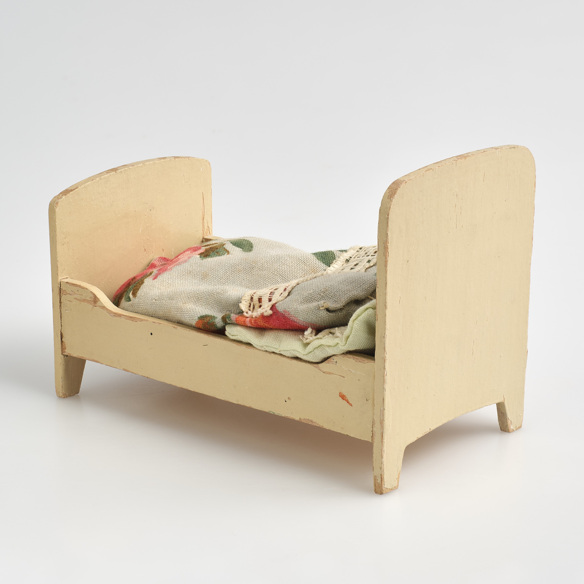 Leketøysseng til dukkehus, tilhørt en lekestue på 1930-tallet.
Sengen består av tre individuelle løse deler; sengeramme, pute og dyne.
Sengerammen er av tre, malt kremhvit, og limt sammen av 5 deler; to endesider, to sengekanter, og en plate. 
Endesiden ved sengens hodeende, er dekorert med et inngravert mønster malt i gull, mønsteret er bygd opp av en trekant øverst i midten, med to korte streker over hverandre på begge sider ut mot kanten, og en større firkant under, uten understrek. Endesiden i fotenden er noe lavere enn ved hodeenden, og dekorert på tilsvarende måte på utsiden. Kantene langs sengen er skjært ut rette, med forhøyning mot endesidene. Alle delene er limt rundt platen som utgjør bunnen av sengen. På undersiden av platen er det skrevet inn en strek med et seks-tall på hver side, med blyant.
Puten er sydd sammen av et lysegrønt stoff, dekorert med et blonde-bånd som streker seg over ca. midten av puten. Puten er generelt preget av misfargin.
Dynen er sydd sammen av et blått blomster-dekorert stoff, og pyntet med samme blonde-bånd som strekker seg over topp-delen av dynen. Formmessig er dynen tilsvarende rektangulær, med en avrundet ende i fotenden.