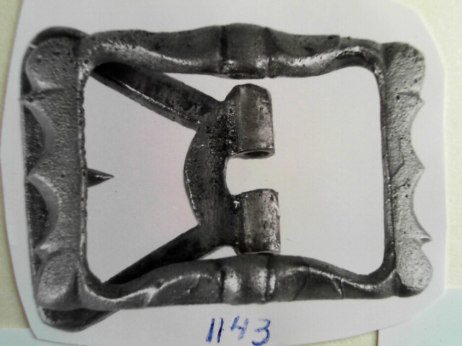 messing. ukjent metall. lær. remmens lengde 2,35 bredde 3. lagt dobbelt. spennen er rektangelformet med ribber. på stolen sitter en sporeformet del med torn i. denne del er av messing. selve spennen er av et blåskimrende metall. :: fra leddiken i kiste Jørgen.