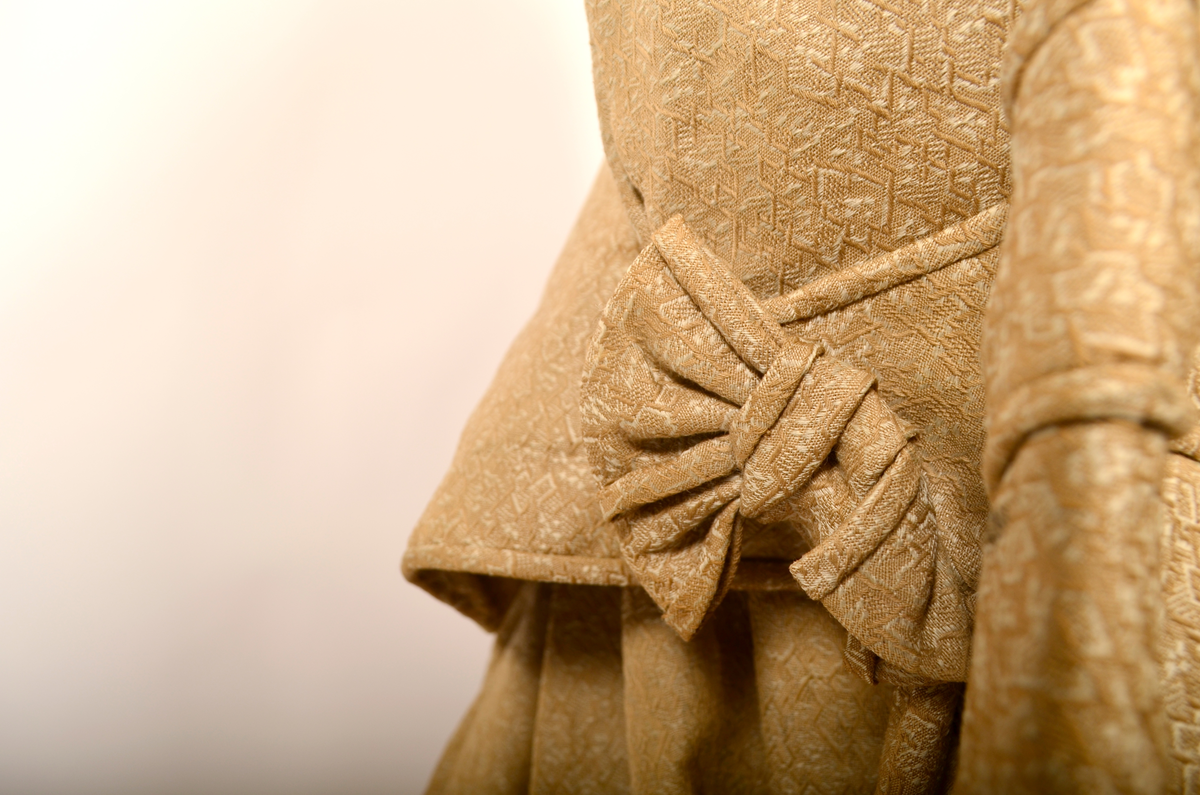 drakt. Fotvidt skjørt. Vid jakke. Fihursydd. Beige mønstret. Kappe på skjørt. Sløyfer på ermer.