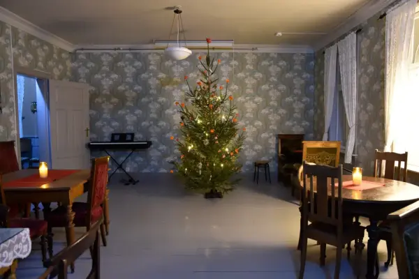 Innendørs bilde med pyntet juletre i midten. Blomstrete tapet og gråmalt tregulv.