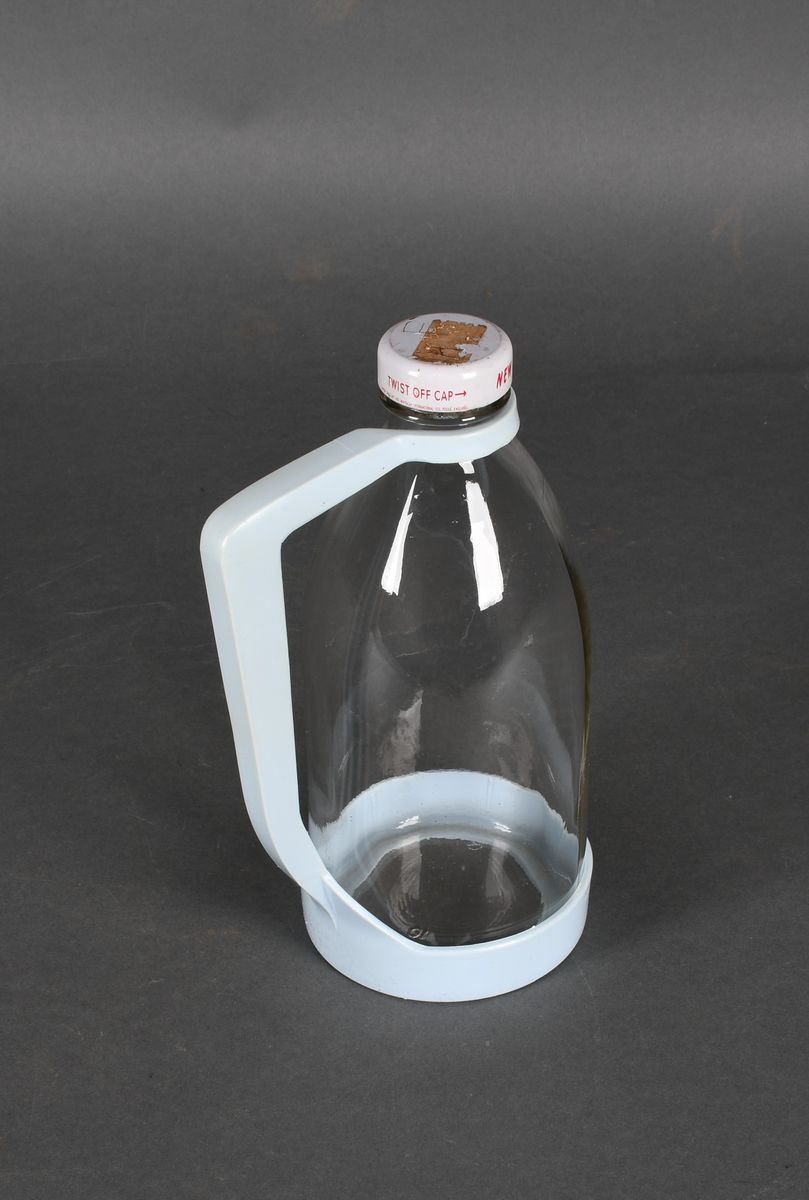 Flaske i klart glass, med lyseblå plastholder og hvit plastkork med rød tekst.