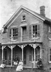 Murhus i to etasjer med forseggjort veranda. To kvinner og t