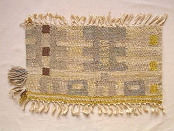 Mattprovet är vävt i rölakansteknik.
Mönstert består av kuber på en linje, mellan kuberna är det vävt
"kammar". Tre linjer fördelas över mattan.Bottenfärgen är grå,
mönstret är i blågrått.

Skiss finns

Mattprovet är vävt på Önnestads mattväveri.