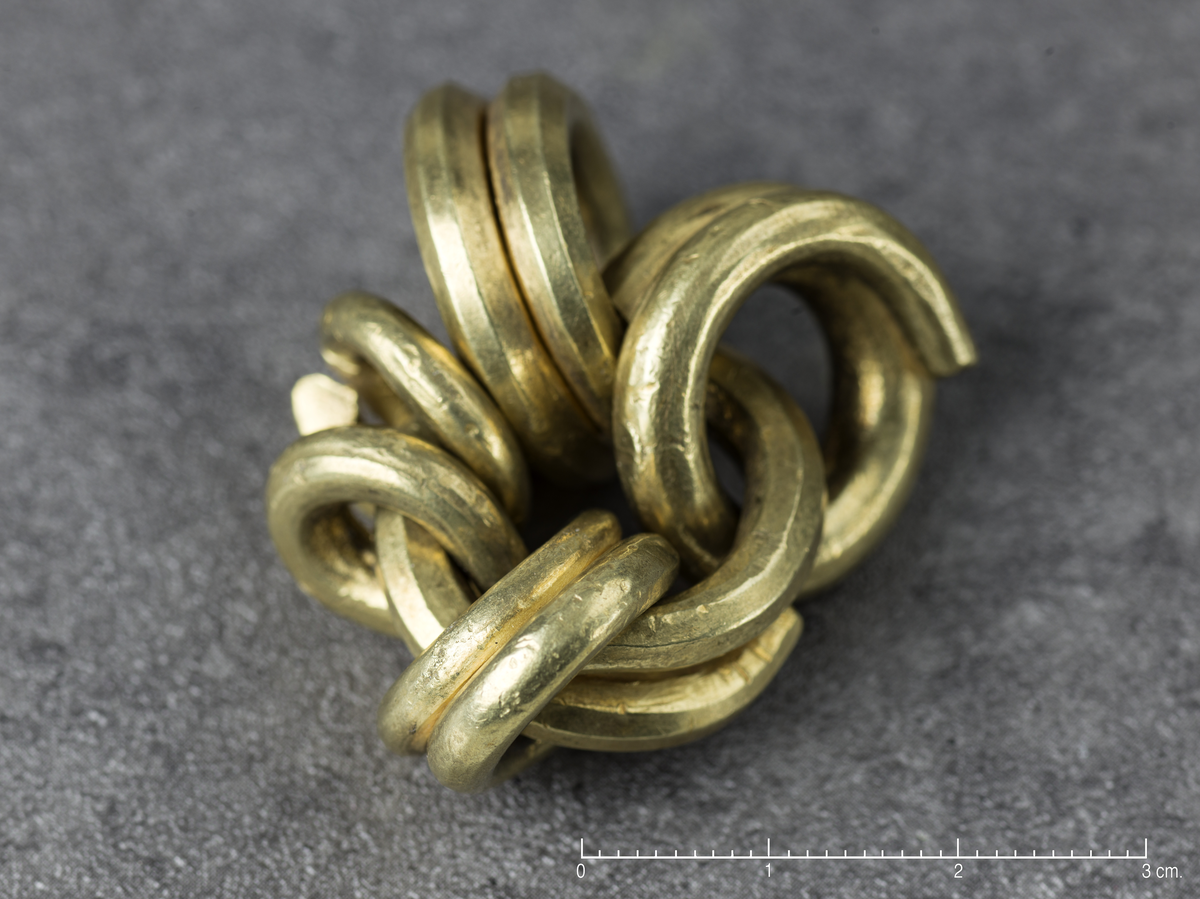 6 betalingsringer av gull, hvorav de fem er hektet inn på den sjette. De fleste av ringene er i et par eller halvannen vinding. Midt ringen har et tverrmål av 2,4 cm., de øvrige fra 2,2-1,6 cm. Bare en av ringene synes å være fullstendig, de andre avkuttet i den ene ende. Et fragment er av finneren av skåret en av ringene og foreligger løst. Samlet vekt 108,208 gr. - 