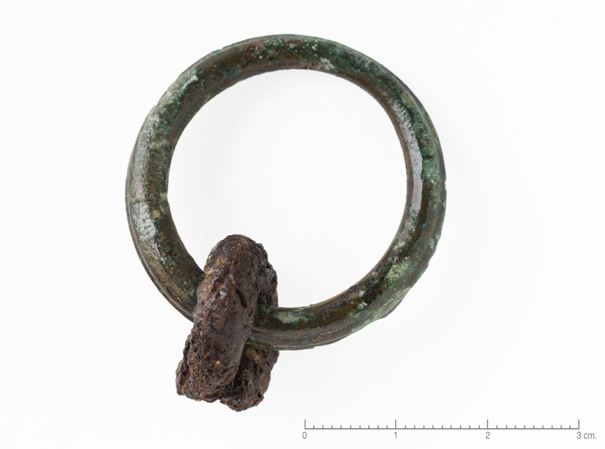 "2547 l. Ring af bronce 3,6 cm i ydre tvermaal. Om ringen gaar en jernbøile." Beltering av bronse med en jernring , diam: 18-20 mm, bøyet rundt bronseringen. Bronseringen har en smal, opphøyet list som løper rundt hele ytterkanten.